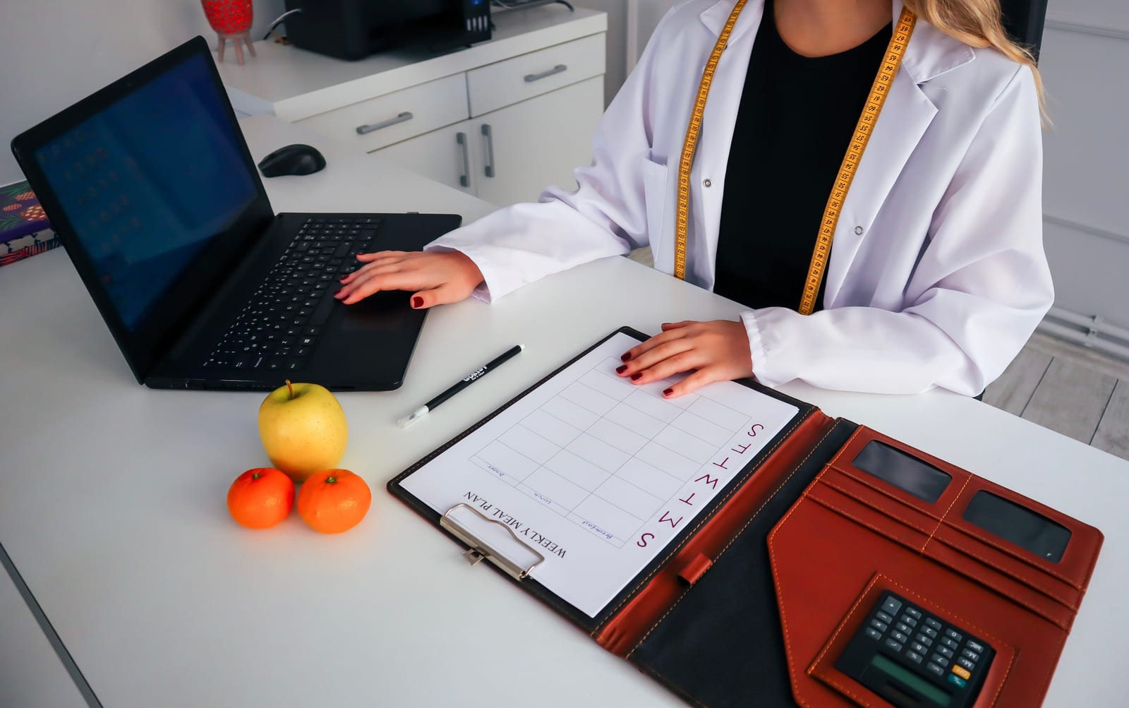 Eine Ernährungsberaterin erstellt an ihrem Laptop einen Essensplan, daneben liegen frisches Obst und ein Kalender.