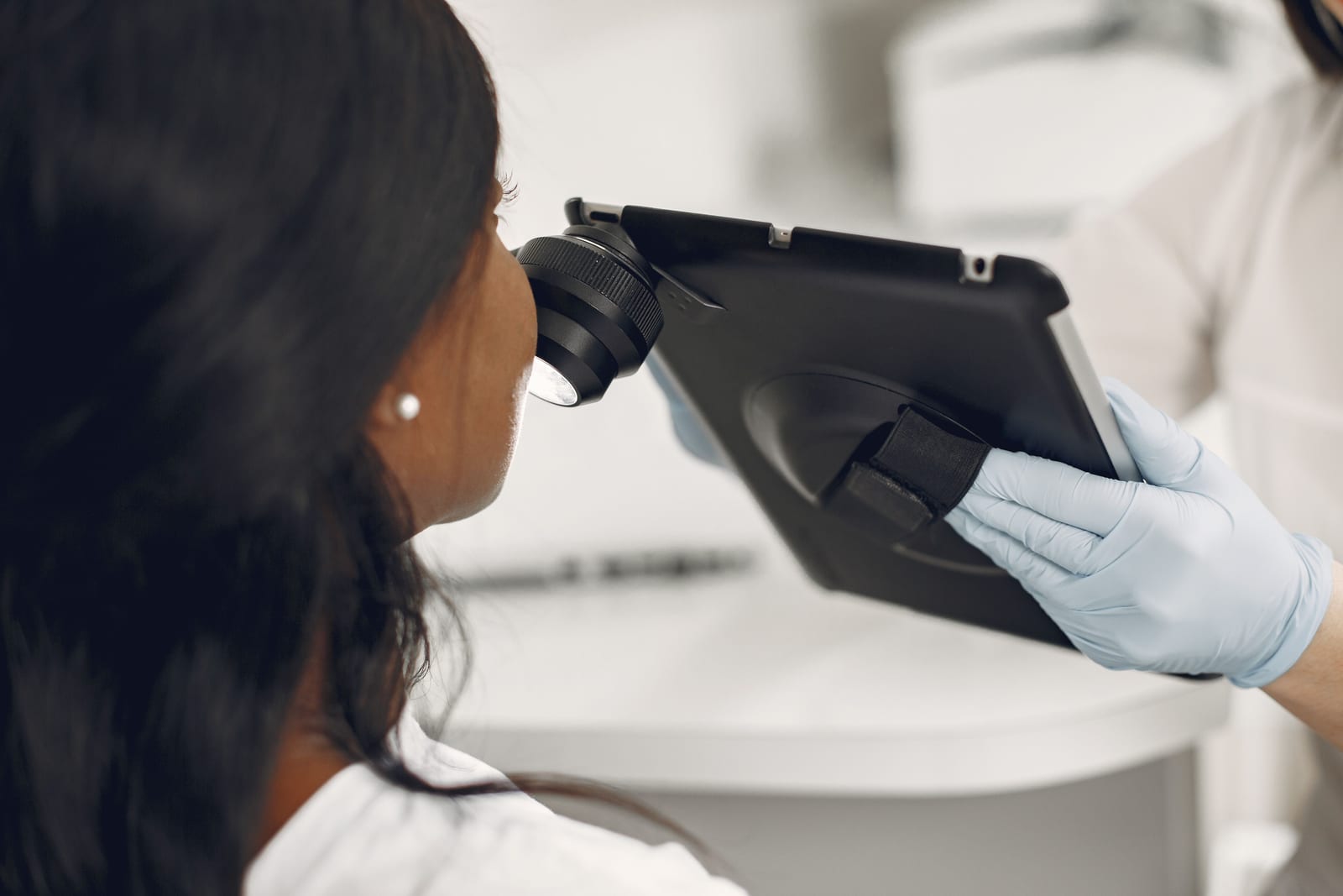 Dermatologe untersucht die Haut einer Patientin mit einem digitalen Dermatoskop und Tablet.
