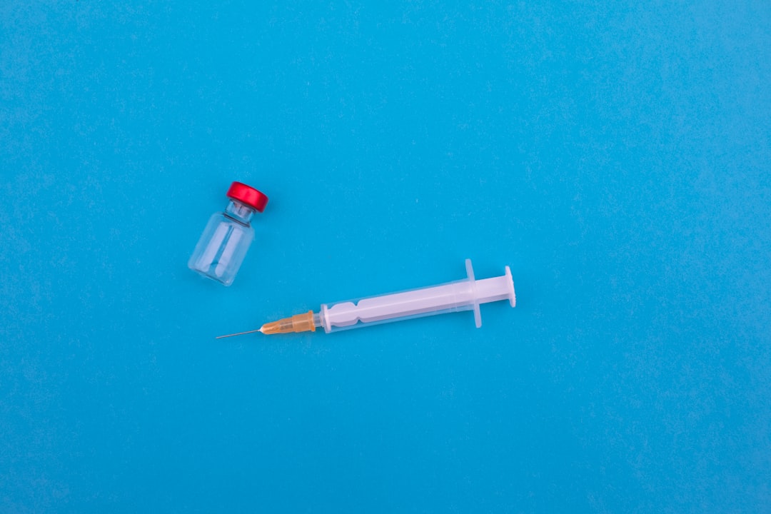 Impfspritze und Impfstoff-Fläschchen mit rotem Deckel auf blauem Untergrund