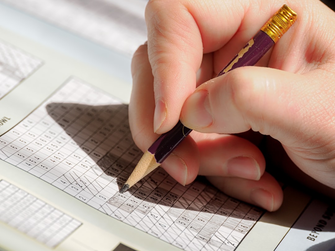 Hand trägt mit einem Bleistift Zahlen in eine gedruckte Tabelle ein