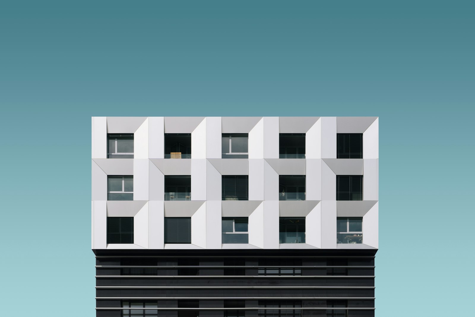 Weiße Wohnhaus-Fassade mit versetzten Balkonkuben vor türkisem Himmel