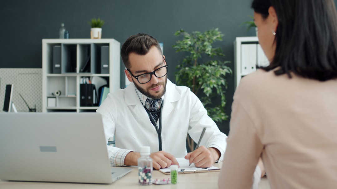 Arzt notiert im Sprechzimmer etwas auf einem Formular, gegenüber sitzt eine Patientin