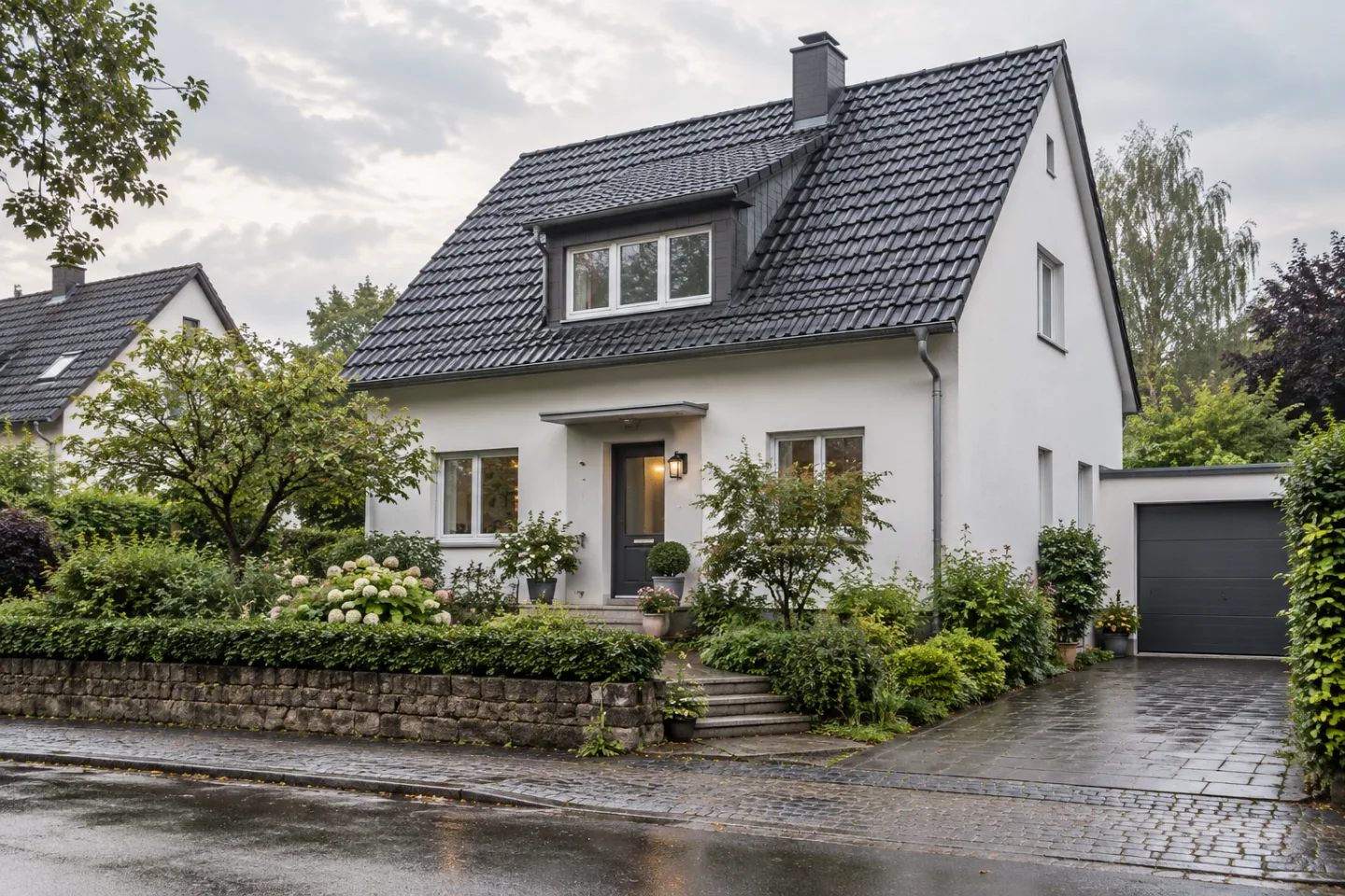 Wohnhaus mit geneigtem Dach, heller Fassade und begrüntem Vorgarten.